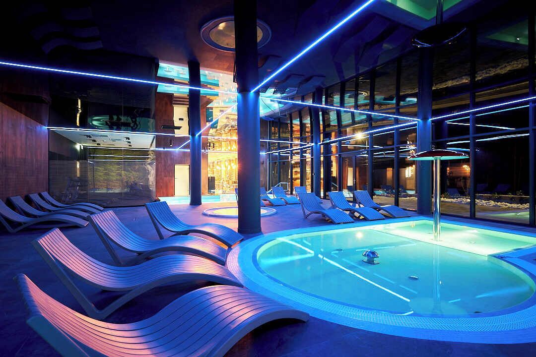 A modern indoor pool area with lounge chairs and a central hot tub.
