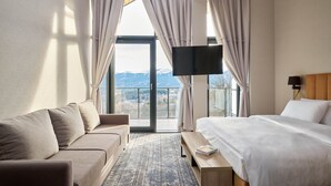 A hotel room with a bed, a sofa, a TV, and a view of mountains. - Złoty Horyzont Resort Szklarska Poręba (Szklarska Poreba)