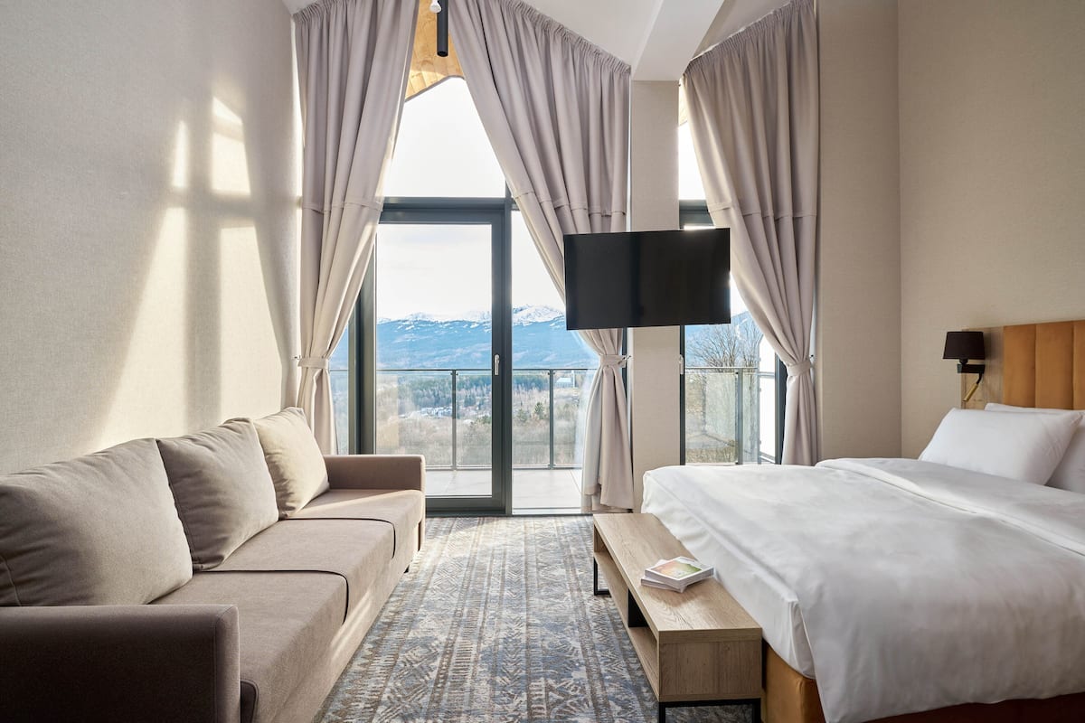 A hotel room with a bed, a sofa, a TV, and a view of mountains.