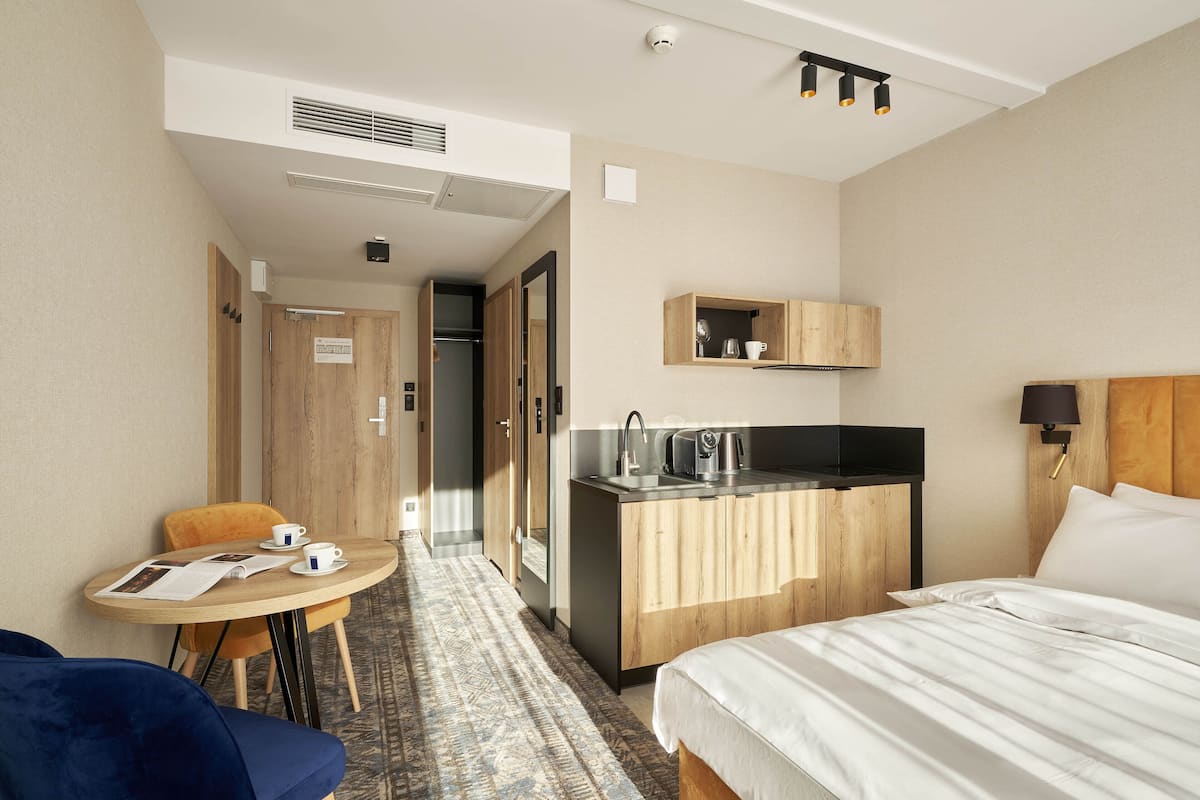 A hotel room with a bed, a small kitchenette, a dining table with chairs, and a separate seating area with a sofa.