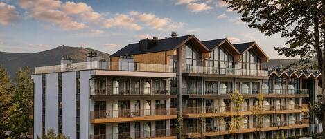 A multi-story hotel with balconies, large windows, and a mountainous backdrop.