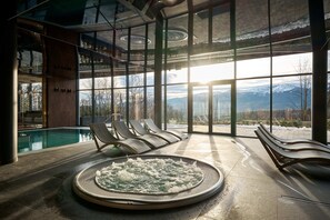 Un área de spa con hidromasaje, sillones de descanso y vistas a montañas a través de amplios ventanales.