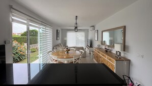 Uma cozinha moderna com uma ilha central, uma área de jantar com mesa redonda e uma grande janela com persianas.