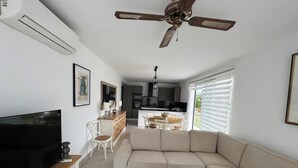 Uma sala de estar moderna com uma televisão de tela plana, uma mesa de centro de madeira, um sofá bege e um ventilador de teto.