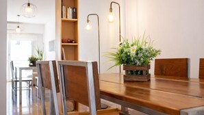 Zona pranzo con tavolo in legno, sedie, una pianta in vaso e una libreria.