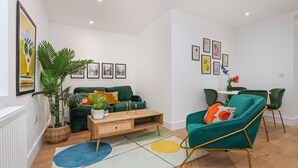 A modern living room with a green sofa, teal armchair, and a coffee table. There are framed pictures on the wall and a potted plant. - Archway luxury interior designed 1 bed (London)