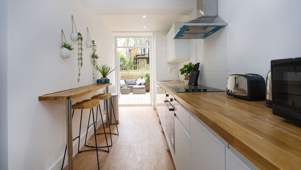 A modern kitchen with a wooden countertop, a built-in oven, and a stainless steel range hood. There are bar stools and hanging plants on the wall. - Archway luxury interior designed 1 bed (London)