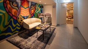 Uma área de estar moderna com um mural abstrato colorido, um sofá, duas poltronas e uma mesa de centro com livros.