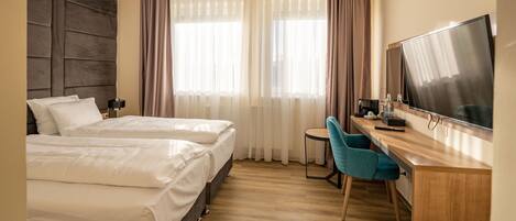 Una habitación de hotel con dos camas, un escritorio, una silla, un televisor y una ventana con cortinas.
