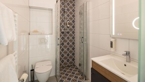 Casa de banho moderna com chuveiro envolto em vidro, sanita e lavatório com espelho.