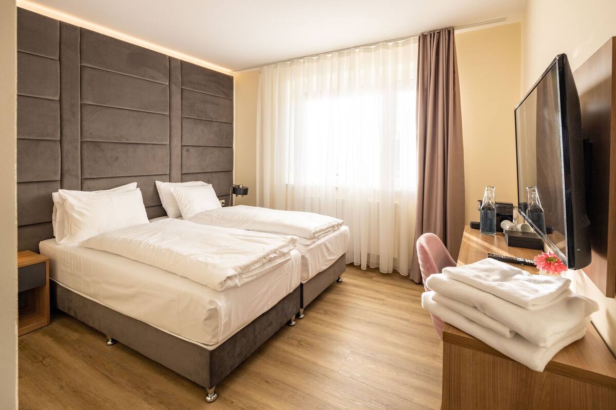 Een hotelkamer met een tweepersoonsbed, een bureau met een televisie en een raam met gordijnen.