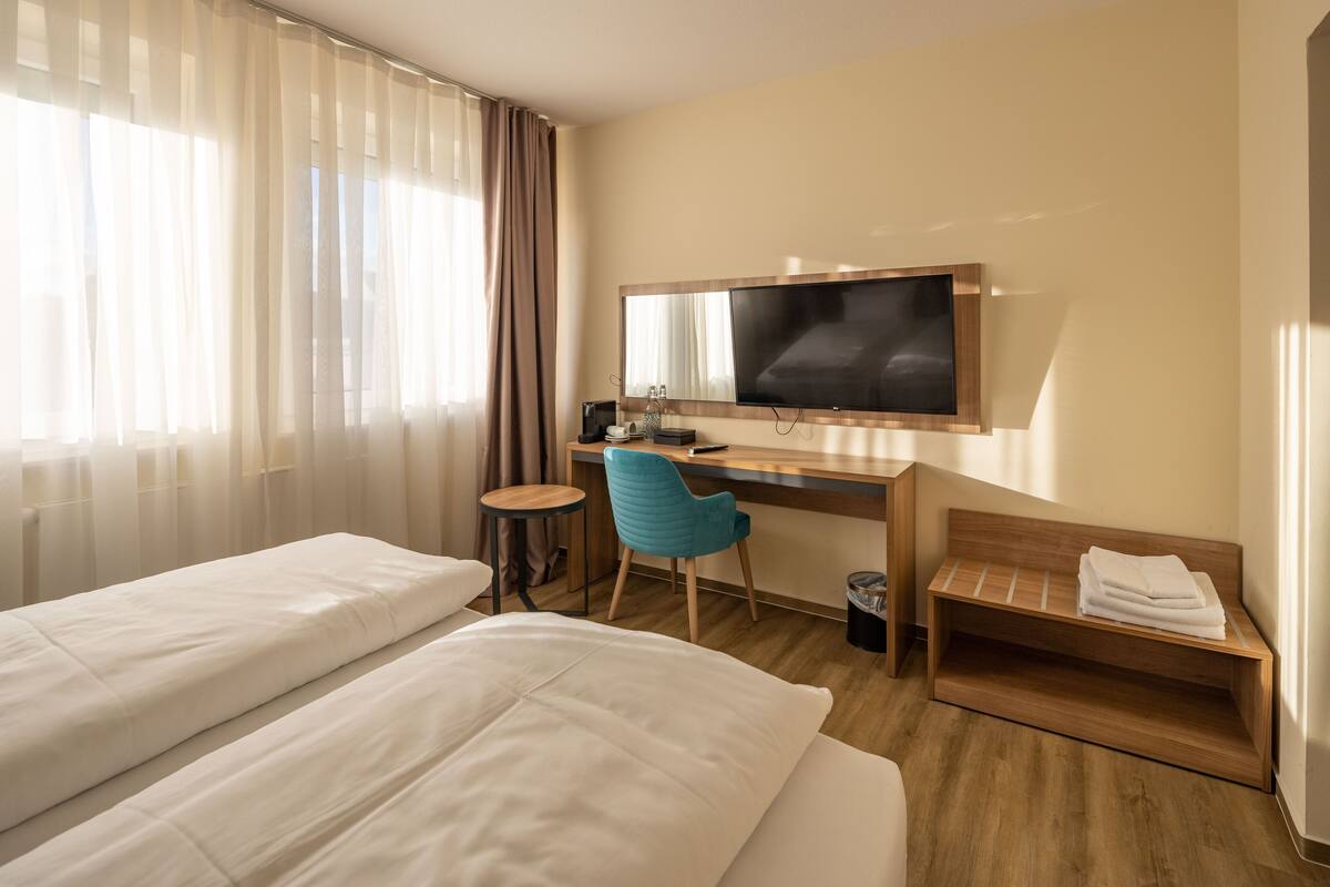 Een hotelkamer met twee bedden, een bureau met stoel, een televisie en een kleine tafel.