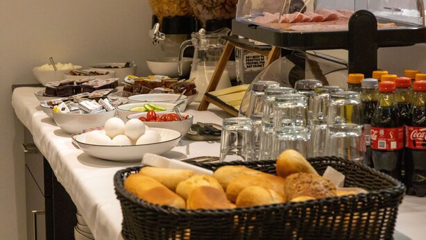 Mesa de buffet com diversos alimentos, incluindo pão, ovos e um display de carne.