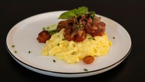 Um prato de ovos mexidos com bacon e uma guarnição de folhas verdes.