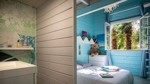 Een slaapkamer met een bed, een raam met gordijnen, een dressoir en een bloemen behang.