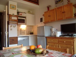 Eine kompakte Küche mit Holzschränken, einem Kühlschrank, einer Mikrowelle und einer Kaffeemaschine.