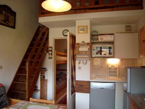 Eine kleine Küche mit Mikrowelle, Kühlschrank und einer Holztreppe, die zu einem Schlafzimmer auf dem Dachboden führt.