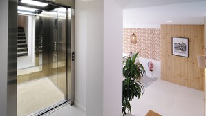Un ascenseur doté d’un écran numérique, un escalier, un espace d’accueil avec un mur revêtu de panneaux en bois, une plante et un extincteur.