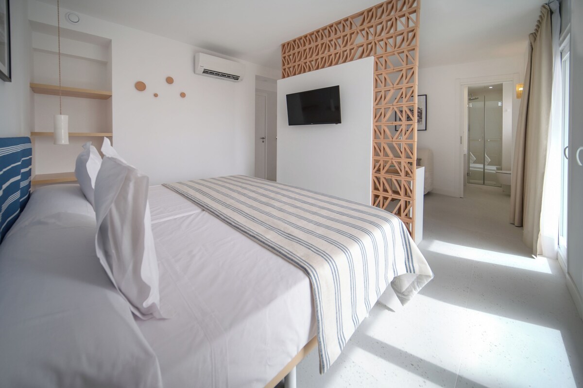 A modern hotel room with a large bed, a TV mounted on the wall, and a wooden partition.