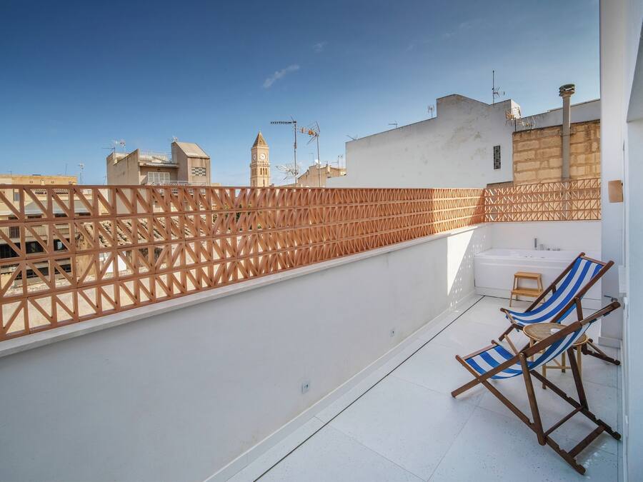 Una terraza en la azotea con un cerramiento de madera, dos sillones de exterior a rayas y una bañera blanca.