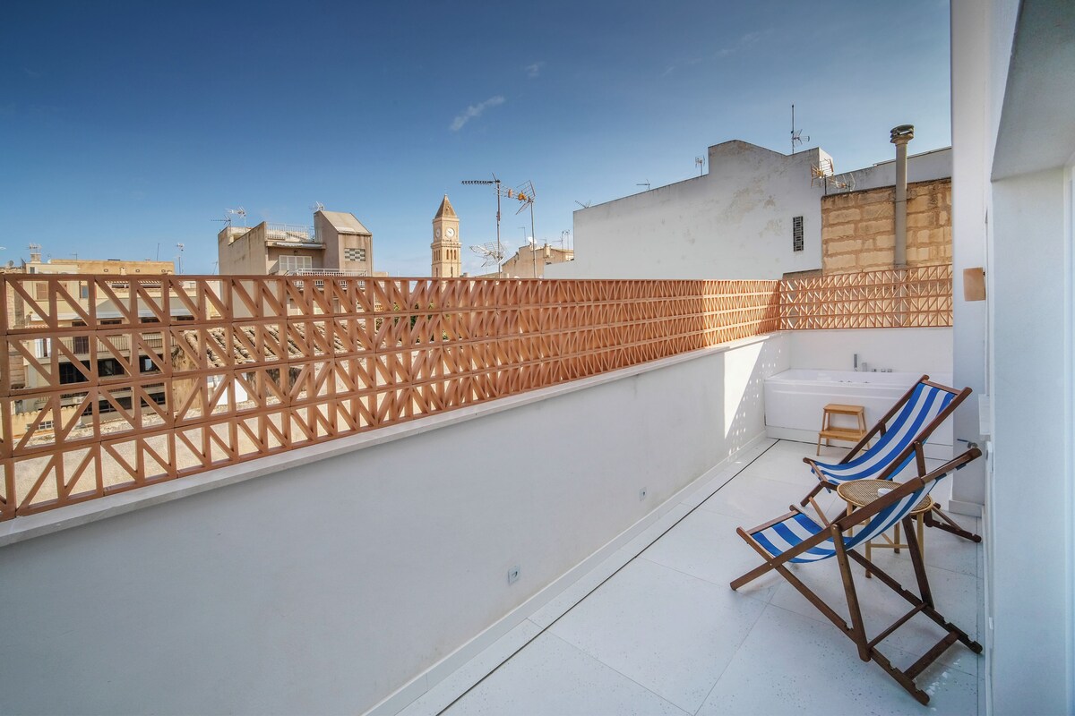 A rooftop terrace with a wooden lattice fence, two striped lounge chairs, and a white bathtub.