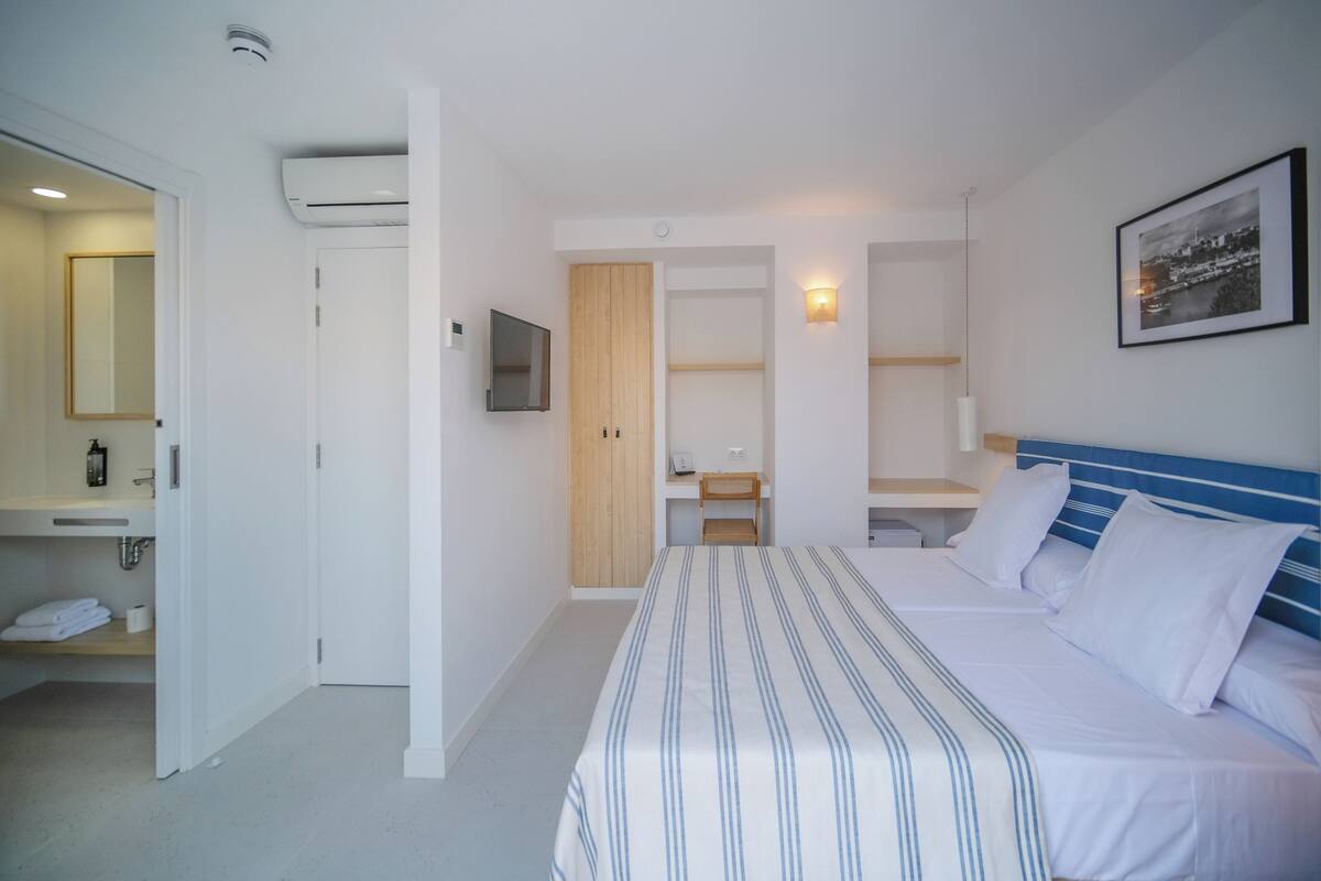 A hotel room with a bed, a desk, a chair, a TV, a wardrobe, and a bathroom with a mirror and towel rack.