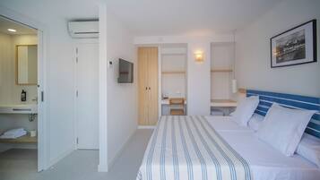 Habitación de hotel con cama, escritorio, silla, televisor, armario y baño con espejo y toallero.