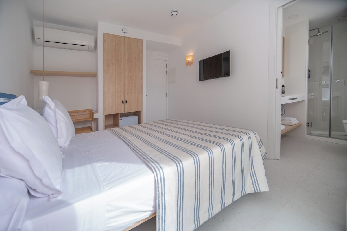A bedroom with a bed, a wardrobe, a television, and a shower area.