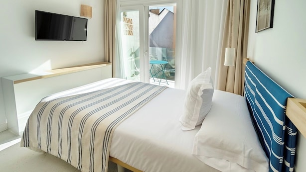 Une chambre d’hôtel avec un lit, un téléviseur fixé au mur, une fenêtre avec des rideaux et une vue sur l’extérieur.