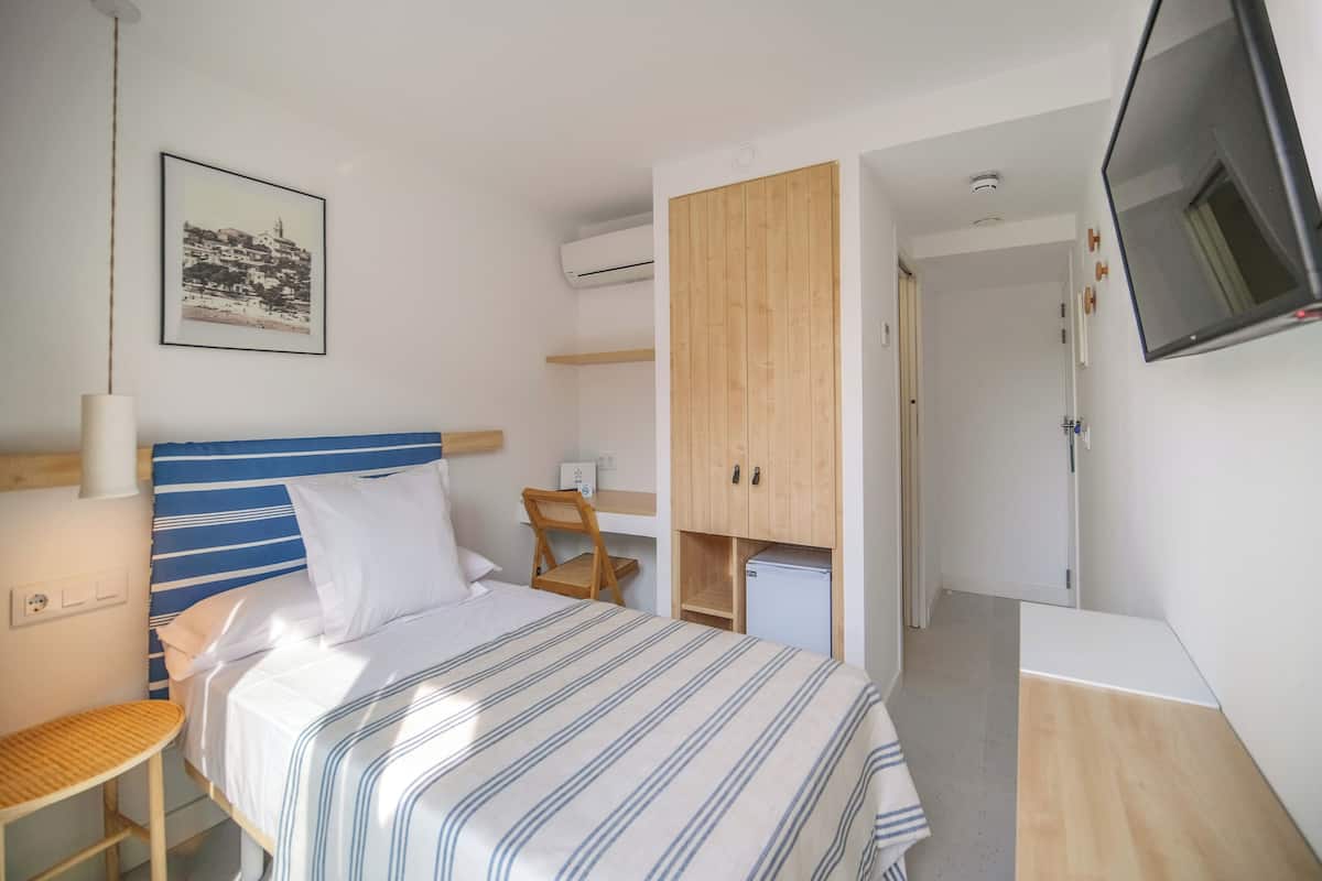 A hotel room with a bed, a desk, a chair, a TV, and a wardrobe.