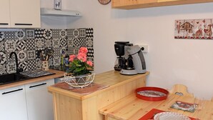 A kitchen with patterned tiles, a coffee maker, and a dining table with a red placemat. - 22m² Studio in Saint-Jean-d'Aulps, near slopes (Saint-Jean-d'Aulps)