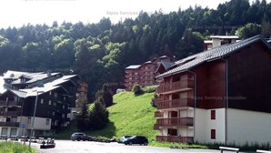 A residential area with multi-story buildings, a parking lot with cars, and a hillside with trees. - 22m² Studio in Saint-Jean-d'Aulps, near slopes (Saint-Jean-d'Aulps)