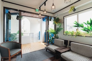 A reception area with a sofa, chairs, a small table, hanging plants, and a view through the glass doors.