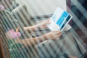 A person reading a book in a room with a window and a plant.
