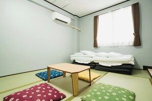 A room with tatami flooring, a futon bed, a small wooden table, and a window with curtains.