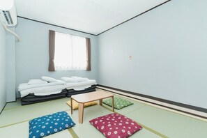A room with tatami mats, a futon bed, a small wooden table, and a window with curtains.
