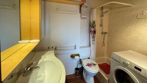 Casa de banho com lavatório, sanita, chuveiro e máquina de lavar roupa.