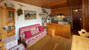 Interior acolhedor de cabana com teto de madeira, sofá com roupa de cama estampada, área de cozinha com armários de madeira e mesa de jantar.