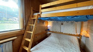 Uma cama beliche com escada de madeira, uma janela com persianas e um abajur.
