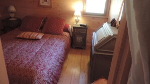 A cozy bedroom with a wooden ceiling, a bed with patterned bedding, a nightstand with a lamp, and a dresser. - Savoyard Chalet 8 pers, near slopes, parking (Crest-Voland)
