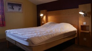 Ein Einzelbett mit Holz-Kopfstück, zwei Wandleselampen und ein gerahmtes Bild an der Wand.