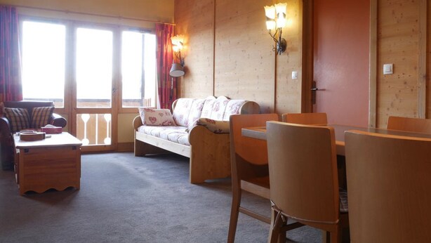 Ein gemütliches Zimmer mit einer Couch, einem Esstisch mit Stühlen, einer Lampe und einem fenster mit Vorhängen.