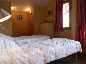 Un dormitorio con dos camas individuales, un armario de madera, una lámpara de pared y un ventanal con cortinas.