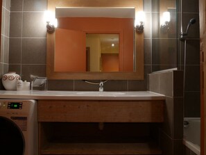 Un baño con tocador de madera, espejo, lavamanos, ducha y lavadora.