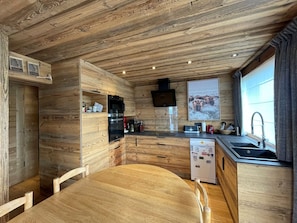Cozinha compacta com paredes de madeira, forno embutido, micro-ondas, frigorífico e janela com vista para animais.
