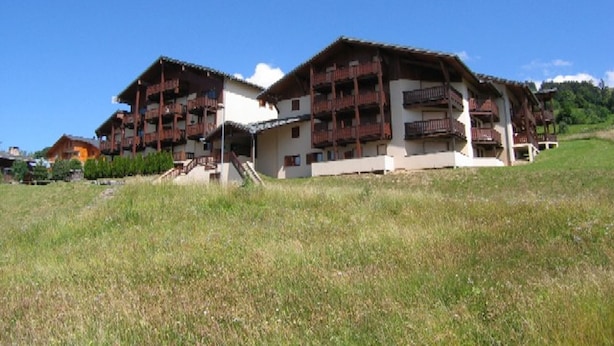 Ein mehrstöckiges Gebäude mit Balkonen, umgeben von einer Wiese und Bäumen.