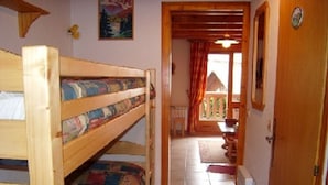 Ein Zimmer mit Etagenbett, einer Tür zu einem Balkon und einem kleinen Tisch mit Stühlen.