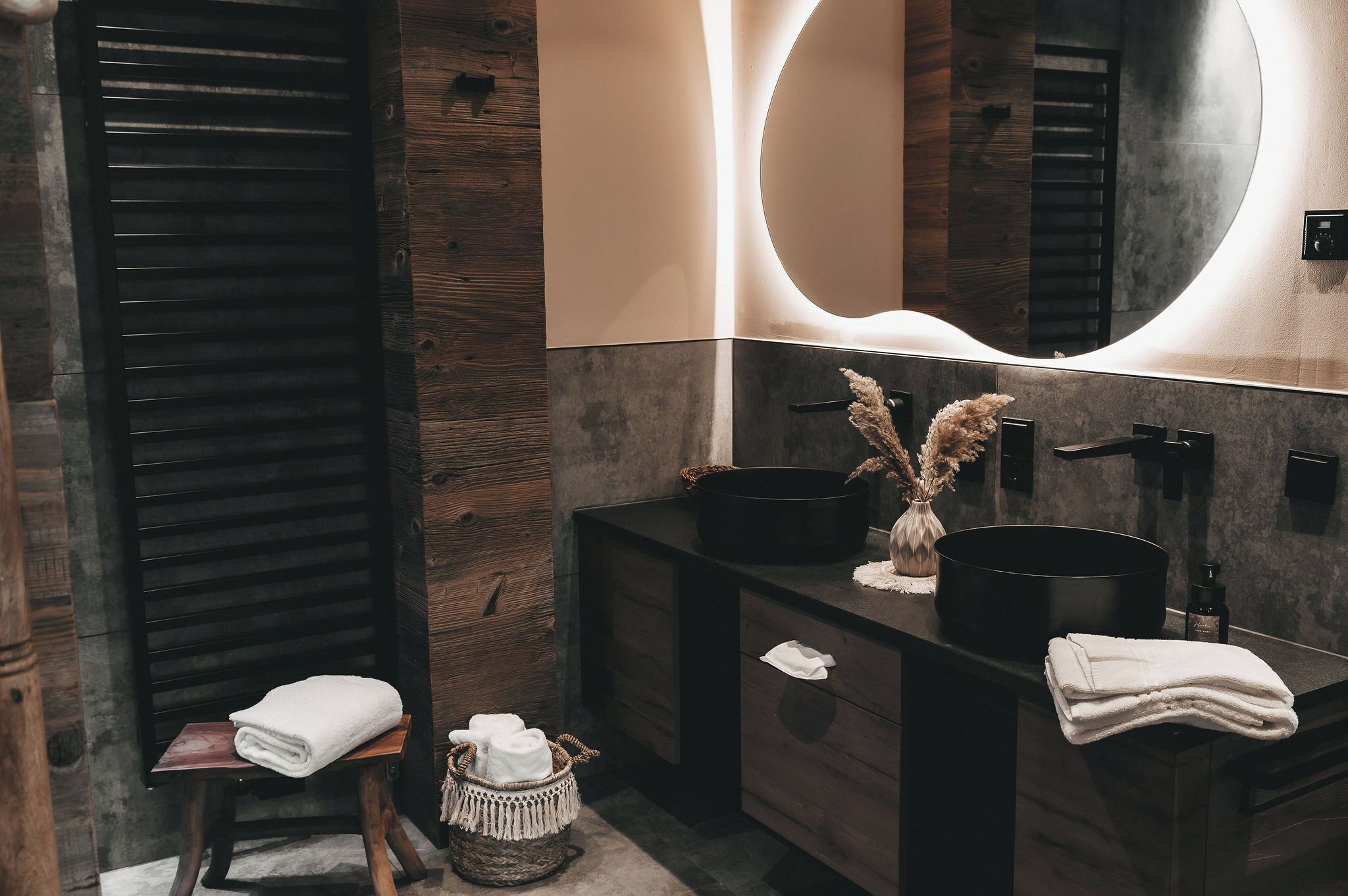 A modern bathroom with a wooden wall, a large mirror, and two black sinks.