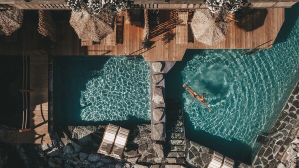 An aerial view of a resort with two swimming pools, wooden deck areas, and stone pathways.