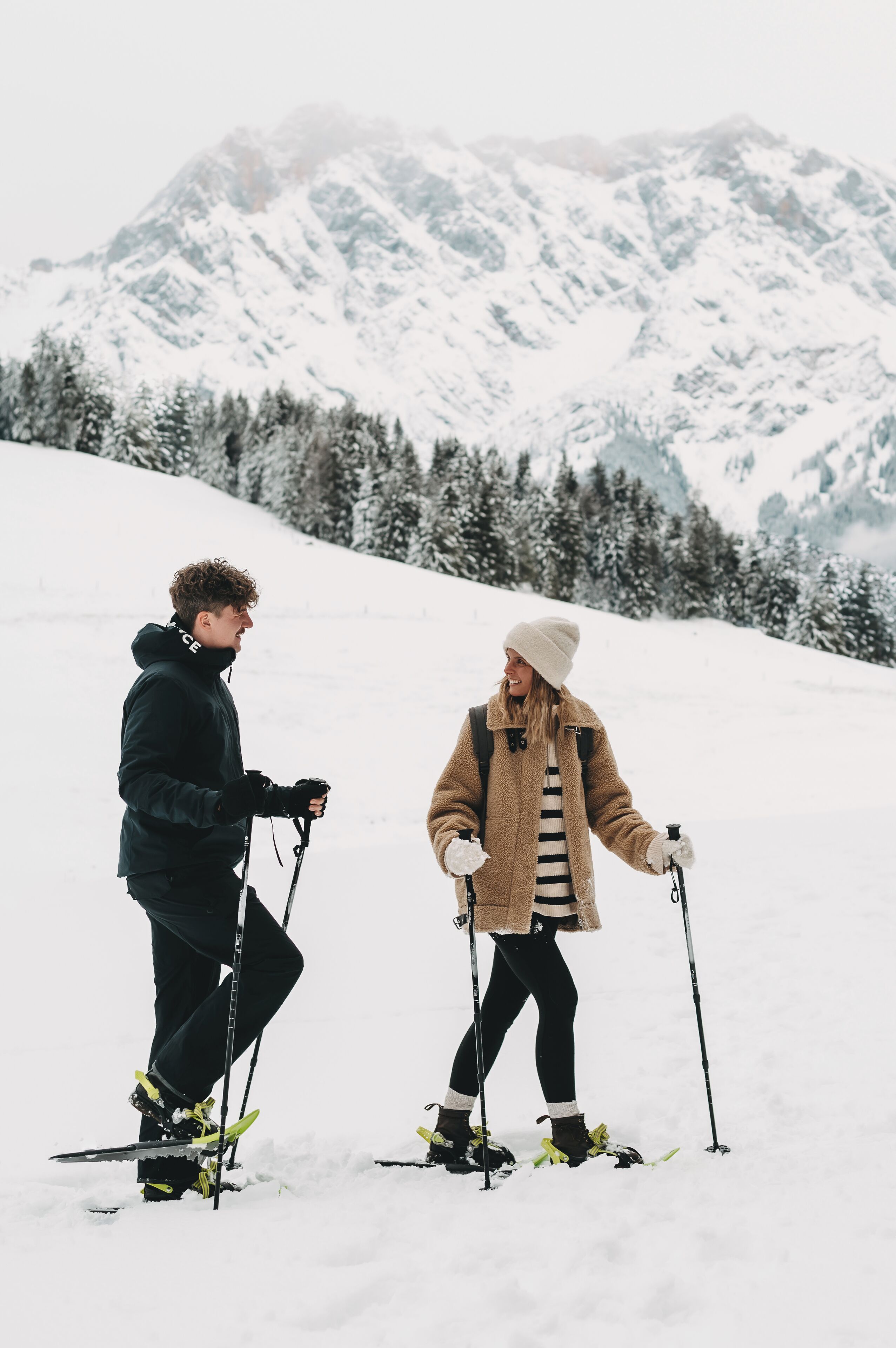 Two people skiing on a snowy mountain with a forested background.